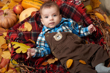 child boy lie on tartan plaid with yellow autumn leaves, apples, pumpkin and decoration, fall season
