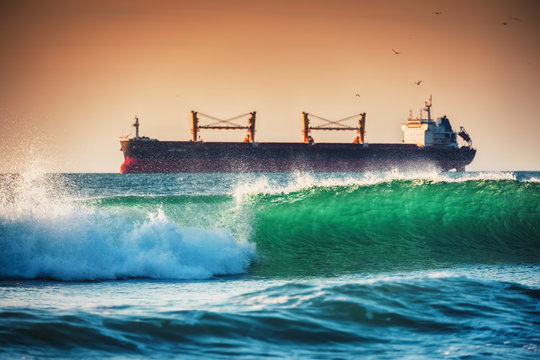 Sea Sunrise, sailing cargo ship and crashing sea waves