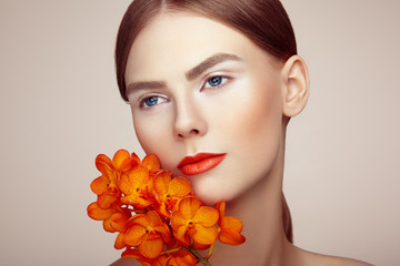 Naklejka premium Portrait of beautiful young woman with orchid. Brunette woman with luxury makeup. Perfect skin. Eyelashes. Cosmetic eyeshadow. Orange flowers