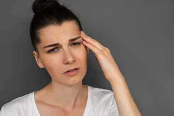 Close up headshot of unhappy young brunette female having frustrated and painful expression, touching temple with hand, suffering from bad headache or migraine while facing stress at work. Healthcare