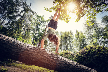 Young man doing a handstand on a tree trunk in the forest.