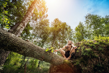 Young man sitting on a tree trunk in the forest.