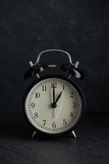 black alarm clock with stone background at one o'clock