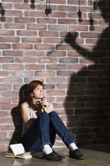 Caucasian girl sitting on the floor reading a horror or scary thriller book. Dramatic lighting with girls eyes wide open and long shadows of woman with knife on the wall near her. Terrified expression