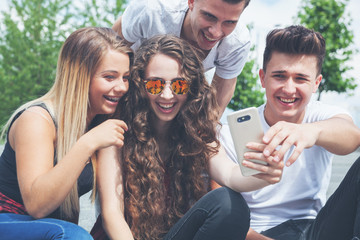 Fototapeta premium Group of friends sitting together using phone and laughing