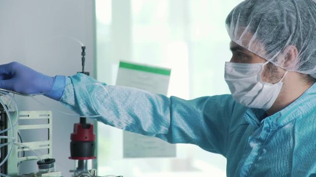 Scientist in a sterile suit (cap, face mask, latex gloves) makes manipulations in chemical laboratory. Laboratory assistant in chemical protection suit works with equipment. Science, biochemistry