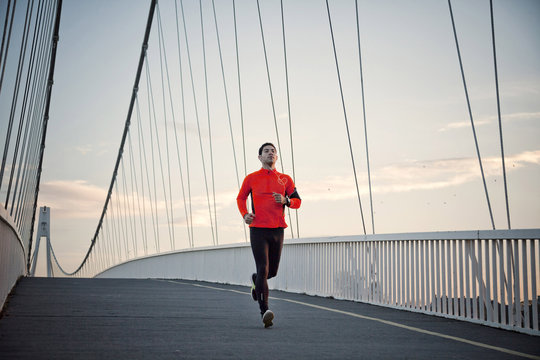 Man with headphones jogging on bridge