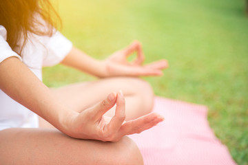 Closeup side view of asian woman meditating in lotus yoga position with sunshine at park. Wellbeing and healthy lifestyle. Health concept.