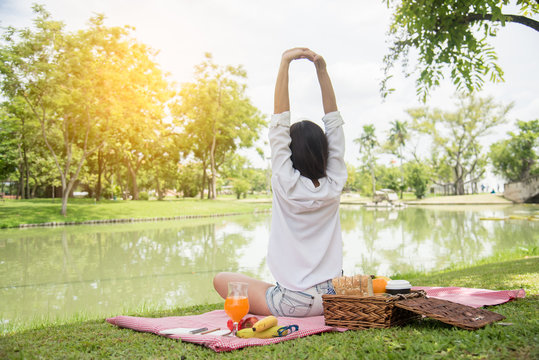 Closeup of young woman streching and relaxing with fruit basket and glass of orange juice in the park at weekend. Wellness. Health and food concept.
