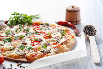Fresh homemade pizza with tomatoes, salami, cheese and mushrooms on piece of baking paper
