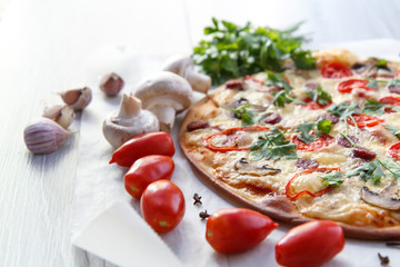 Fresh homemade pizza with tomatoes, salami, cheese and mushrooms on piece of baking paper