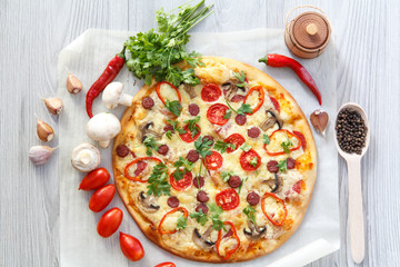 Fresh homemade pizza with tomatoes, salami, cheese and mushrooms on piece of baking paper