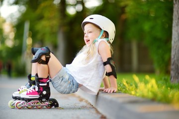 Pretty little girl learning to roller skate on beautiful summer day in a park