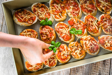 Chef preparation italian food - garnishing bruschetta with roasted tomatoes, basil and cheese, cooking homemade appetizer for the party