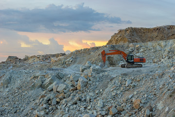 The tracked excavator is parked in the stone quarry after work until the twilight time. - obrazy, fototapety, plakaty