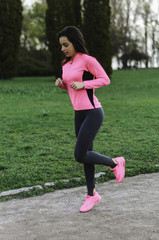 Girl beautiful brunette. Athletic body , pumped muscles. Bright colors , green ,pink . Spring , trees in bloom. She does exercises on the beach , running.