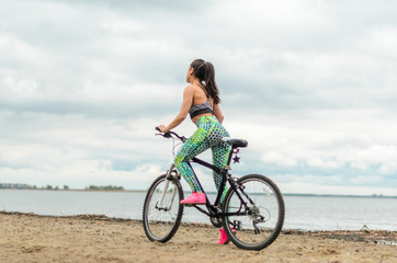 Fototapeta na wymiar The girl the brunette plays sports on the seashore - on the beach. Rides a bike.