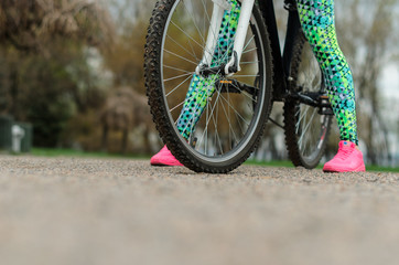 the girl the brunette in sportswear, rides a bike in the morning in the park. Close up a leg, water...
