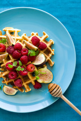 Healthy breakfast: Belgian waffles with raspberries, honey and figs decorated mint leaves on turquoise napkin. Selective focus. Close up