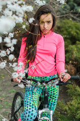 Fototapeta premium Girl beautiful brunette. A sports body, having pumped up muscles. Bright colors, green, pink. Spring, trees in bloom. She does exercises.
