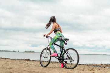 Fototapeta na wymiar The girl the brunette plays sports on the seashore - on the beach. Rides a bike.