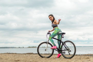 Fototapeta premium The girl the brunette plays sports on the seashore - on the beach. Rides a bike.