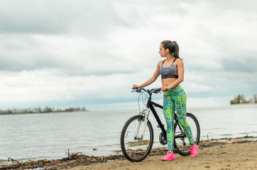 Fototapeta premium The girl the brunette plays sports on the seashore - on the beach. Rides a bike.