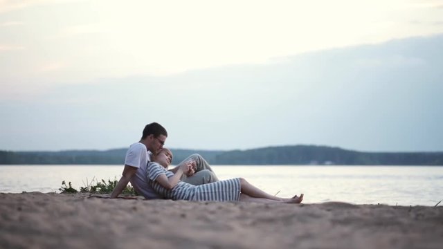 Beautiful young couple sitting on the shore of the river and using the smartphone. Man and woman resting on the beach.