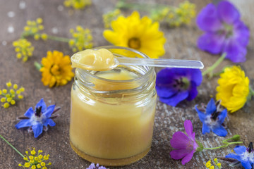 raw organic royal jelly in a small bottle with litte spoon on small bottle surrounded by flowers © JPC-PROD