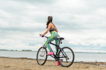Obraz premium The girl the brunette plays sports on the seashore - on the beach. Rides a bike.