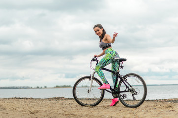 Fototapeta premium Dziewczyna brunetka uprawia sport nad brzegiem morza - na plaży. Jeździ na rowerze.