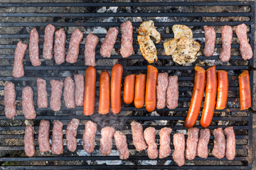 Flat lay above minced meat kebabs and sausages frying on the barbecue grill
