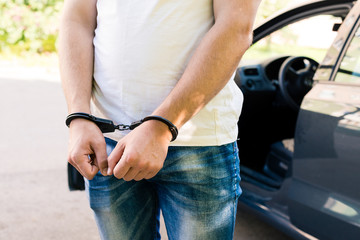 an offender standing in handcuffs near the car. Concept of arrest the driver, violation of rules...