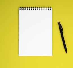 open notepad on the spiral with a clean white page and pencil on a bright yellow background color