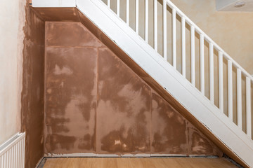 Freshly plastered wall under staircase in a domestic room.