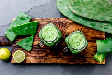 Healthy cactus nopales, aloe vera and lemon detox drink in jars and ingredients on gray background....