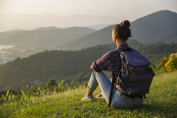 Hipster young girl with backpack enjoying sunset on peak mountain. Tourist traveler on background...
