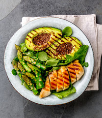 Healthy grilled chicken, grilled avocado and asparagus salad with linen seeds. Balanced lunch in bowl. Gray slate background. Top view