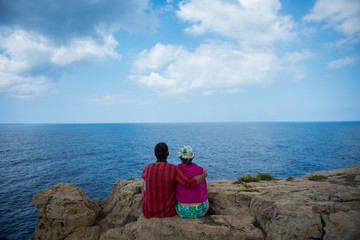 Fototapeta na wymiar Romantic couple sitting on a cliff and admirig wonderful seascape