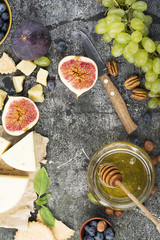 Cheese board for snacks, tricks, meetings with friends, on a gray stone background: assorted cheeses, young cheese, parmesan, cheese with fenugreek, figs, nuts, honey, grapes. Top View.