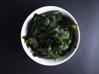 Japanese wakame seaweed soaked in water, placed in small bowl and isolated on black background