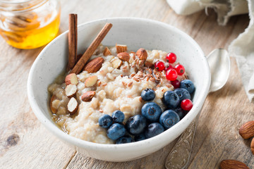 Oatmeal porridge with blueberries, almonds, cinnamon, honey, linseed and red currants in bowl. Healthy breakfast food