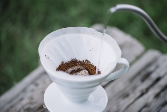 Delicious pourover coffee blossoming while man pours water into the dripper on the ground coffee beans. Summer picnic on the old wooden table background