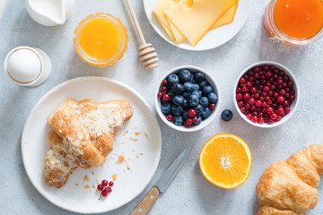 Continental breakfast table top view. Fresh croissants, boiled egg, cheese, orange, jam, honey, blueberries and currants on bright blue table. Horizontal