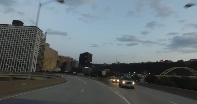PITTSBURGH, PA - Circa September, 2017 - A rear driving perspective on the Fort Duquesne Bridge at dusk with the Pittsburgh city skyline in the distance.  	