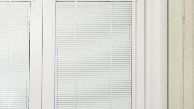 White horizontal blinds and rolled curtain at a window with a frame from white plastic