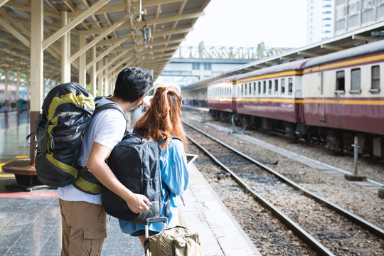 Couple traveler searching right direction at train station.Asian Backpackers pointing and planning holiday vacation with gps map in tablet.Travel concept.