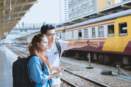 Couple asian woman and asian man traveler pointing and looking out with train station background. Travel in summer concept