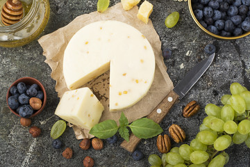 Young white cheese, a new recipe for cheese with fenugreek, a hard chopped Parmesan on a gray stone background with blueberries, nuts, green grapes, honey. Top view. Selective focus..