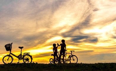 Silhouette biker lovely family at sunset over the ocean.  Mom and daughter bicycling at the beach.  Lifestyle Concept.